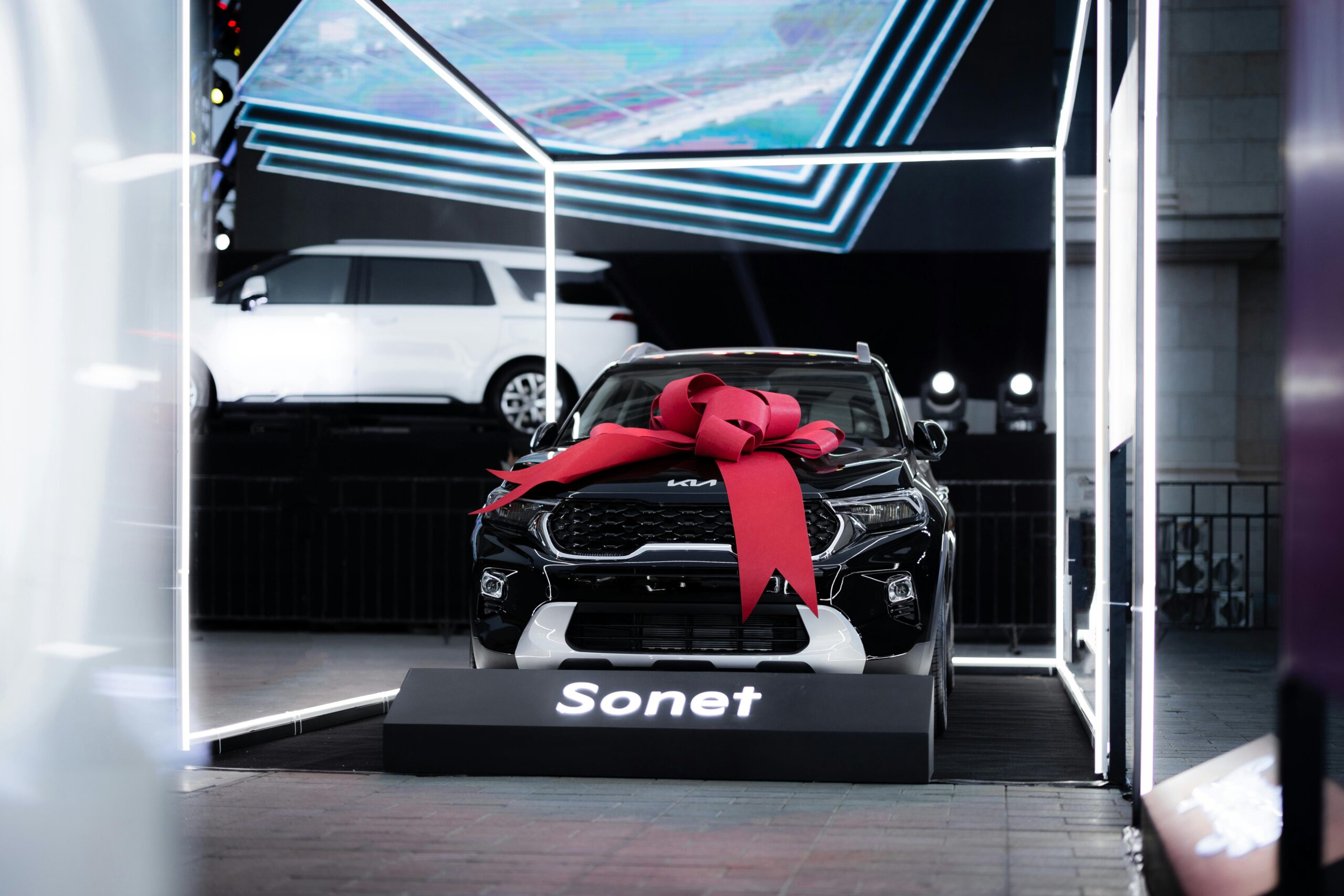 A black Kia Sonet with a red bow on display indoors, highlighting luxury and modern design.